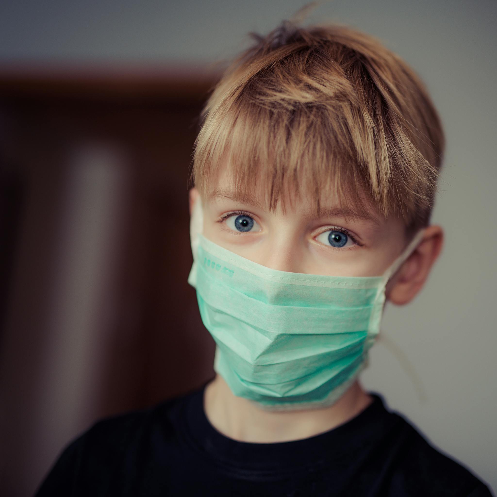 Young boy with bright eyes wearing a protective mask indoors.
