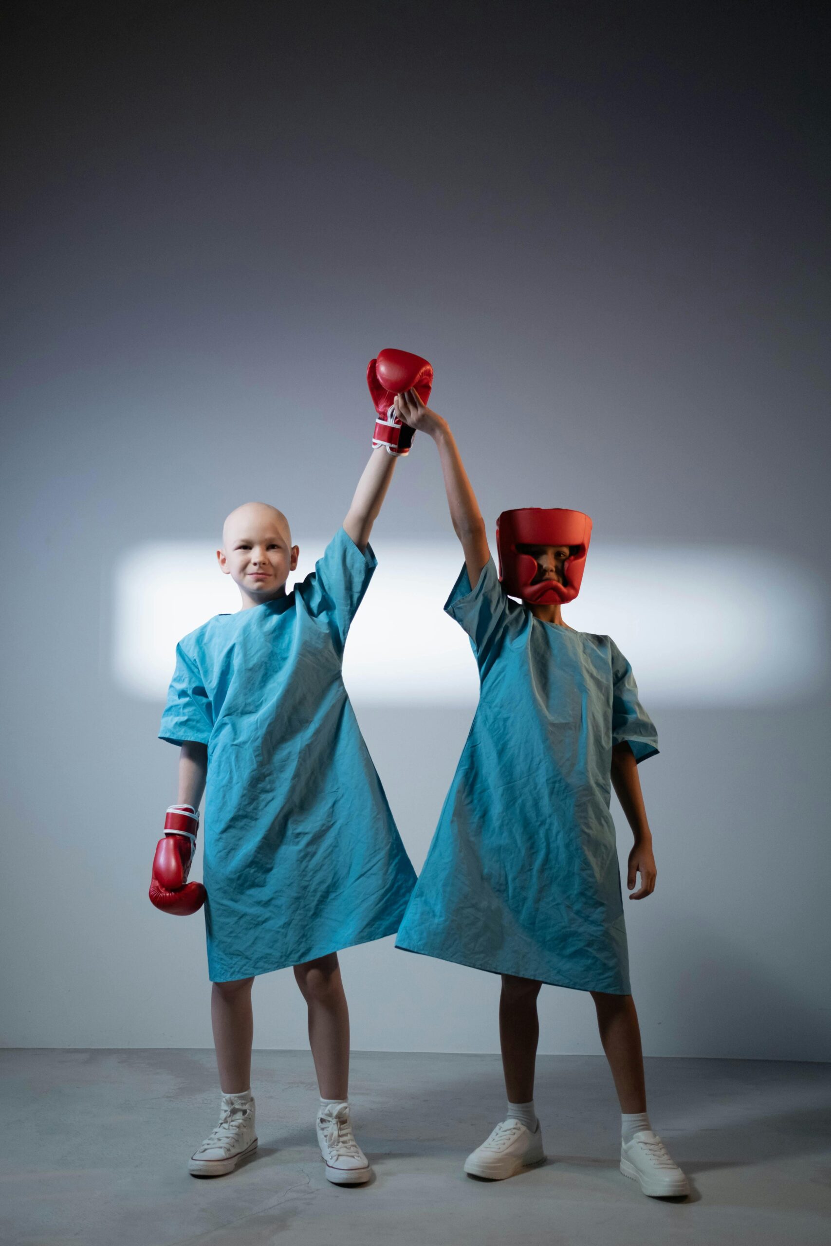 Two children in hospital gowns posing with boxing gloves showing strength and resilience.